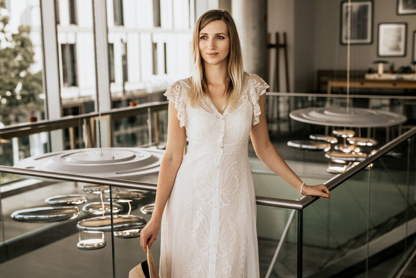 白いドレスを着た金髪の女性の肖像。美しい女の子はレストランで階段の近くに滞在 - 写真・画像