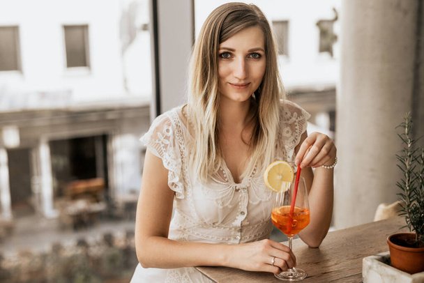 Smiling attractive woman wearing white dress indoor. Young woman take alcohol cocktail - Photo, Image