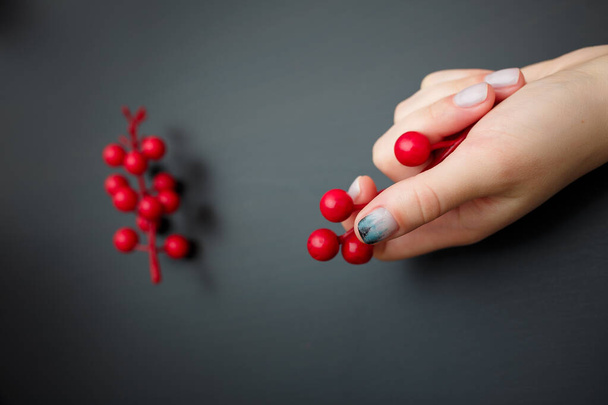 黒い背景に赤い果実を保持モミの木の森マニキュアを持つ女性の手。クリスマスや冬のネイルアート。手のケア、爪のデザイン、美しさと健康の概念。スペースのコピー. - 写真・画像