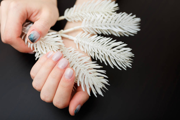 Vrouwelijke handen met sparrenboom manicure houden witte kunstmatige sparren tak op zwarte achtergrond. Kerst of winter nagel kunst. Handen zorg, vingernagels ontwerp, schoonheid en gezondheid concept. Kopieerruimte. - Foto, afbeelding