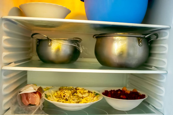Prateleiras de um refrigerador de geladeira aberto com comida diferente, comida cozida em panela e recipiente de plástico. - Foto, Imagem