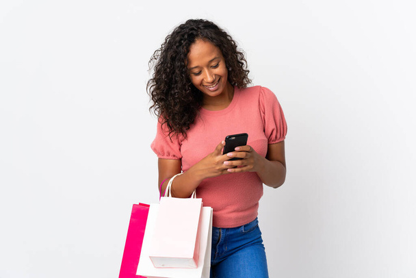 Дівчина-підліток кубик ізольована на білому тлі тримає сумки для покупок і пише повідомлення зі своїм мобільним телефоном другу
 - Фото, зображення
