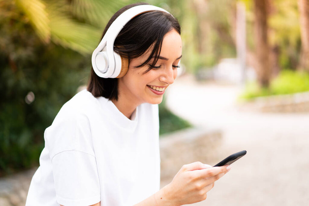 Mujer joven escuchando música al aire libre - Foto, Imagen