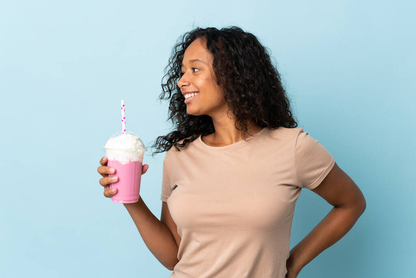 Teenager girl  with strawberry milkshake isolated on blue background looking side - 写真・画像