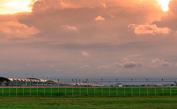 Paesaggio di prato verde e recinzione dell'aeroporto e bel cielo al tramonto. Aereo commerciale parcheggiato al grembiule dell'aeroporto. Coronavirus ha avuto un impatto sul settore dell'aviazione. Recinzione per sicurezza e protezione. - Foto, immagini