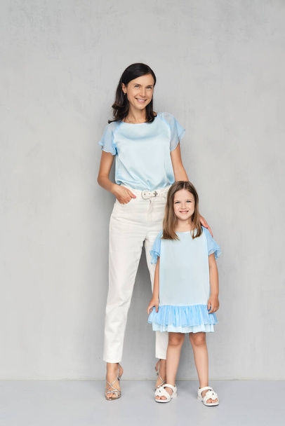 Elegante y de moda madre y su hija posando juntos cerca de la pared gris
 - Foto, imagen