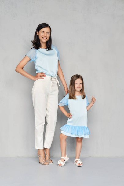 Stylish and trendy mother and her young daughter posing together near gray wall - Photo, Image