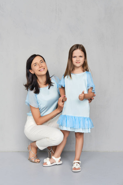Stylish and trendy mother and her young daughter posing together near gray wall - Фото, изображение