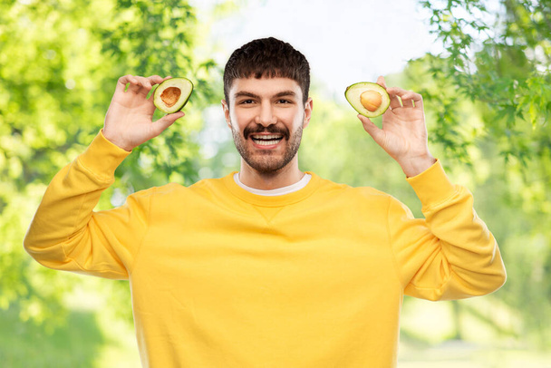 happy young man in yellow sweatshirt with avocado - Fotoğraf, Görsel