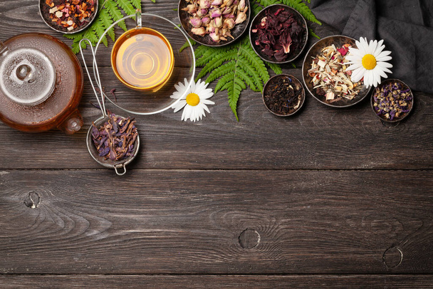 Különböző gyógynövény száraz tea, teáskanna és csésze fa asztalon. Felülnézet fénymásoló felülettel. Lapos fektetés - Fotó, kép
