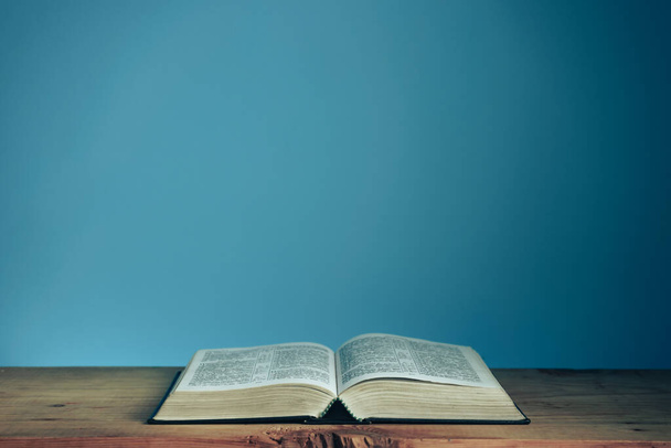 Open Holly Bible on a red wooden table. Beautiful blue wall background. Religious concept. - Photo, Image