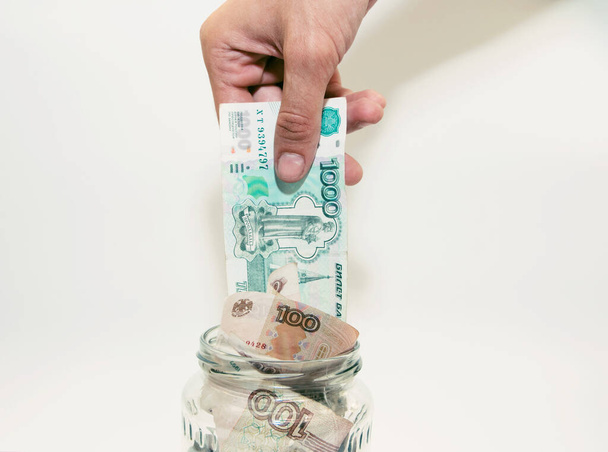 a man puts a bill in a glass jar filled with paper money - Fotó, kép