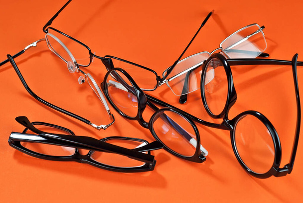Different types of glasses on an orange background close up. Glasses with rectangular and round frames. - Foto, imagen