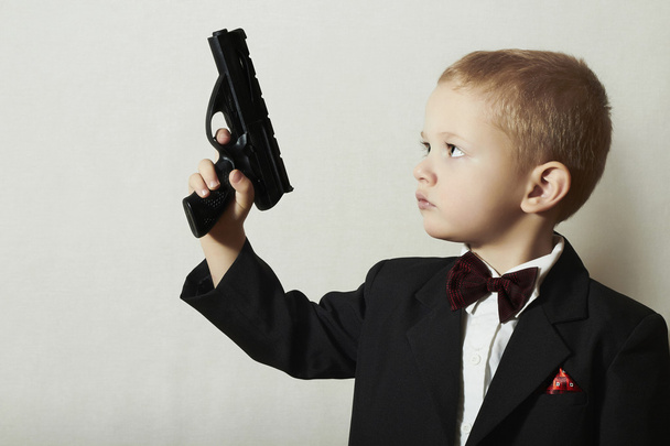 wenig James Bond. modischer kleiner Junge in Fliege. Stilvoller Agent. Modekinder. 4-jähriges Kind im schwarzen Anzug. Eleganz schöner Junge mit Waffe. - Foto, Bild