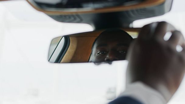 Primer plano ajustando el espejo retrovisor en el coche. Hombre africano sentado frente al coche
 - Foto, imagen