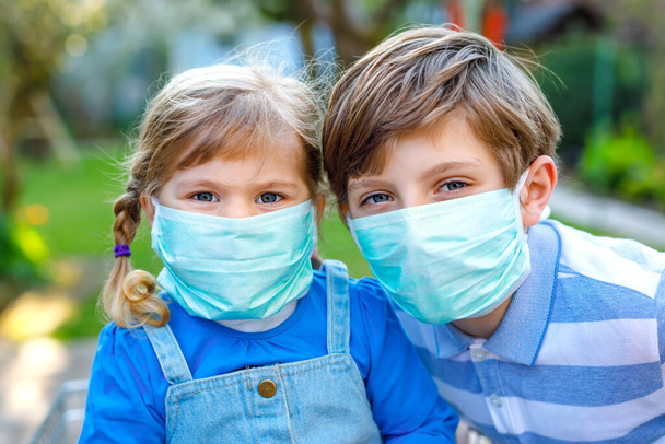 Twee kinderen, klein peutermeisje en schooljongen met medisch masker als bescherming tegen een pandemische coronavirusziekte. Kinderen broers en zussen met winkelwagentje met behulp van beschermende apparatuur als gevecht met covid 19. - Foto, afbeelding