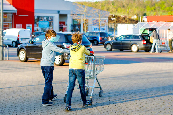 Twee jongens met een medisch masker als bescherming tegen een pandemische coronavirusziekte. Kinderen die beschermende uitrusting gebruiken tegen covid 19 en gaan winkelen in de supermarkt met karretje trolley. - Foto, afbeelding