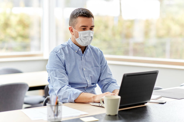 man in mask with laptop working at home office - Photo, Image