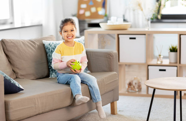 happy little girl with apple sitting on sofa - Zdjęcie, obraz