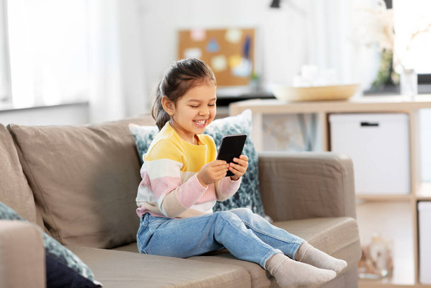 happy smiling little girl with smartphone at home - Photo, Image