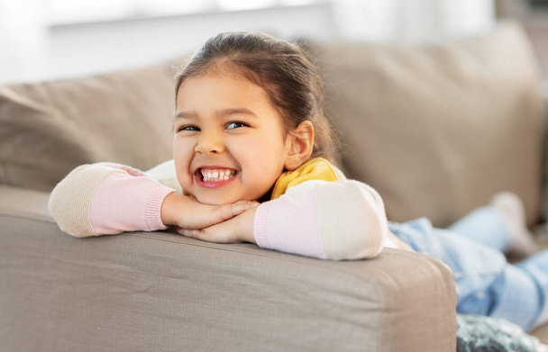 happy smiling little girl lying on sofa at home - Valokuva, kuva
