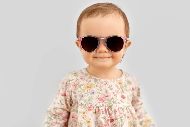 happy little baby girl in sunglasses over grey - Foto, afbeelding