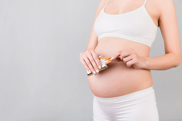 Cropped image of a pack of cigarettes at gray background. Bad habbit of a pregnant woman in white underwear. Careless mother. - Photo, Image