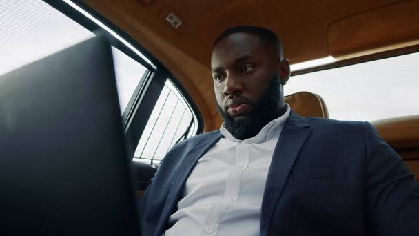 アフリカの男はノートパソコンの画面を見て。車の中でコンピュータを操作するビジネスマン - 写真・画像