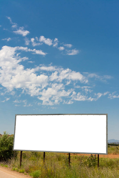 One billboard next to a road in the field and blue sky with clouds. Vertical image with horizontal white copy space. - Photo, Image
