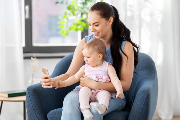 gelukkig moeder en baby met smartphone thuis - Foto, afbeelding