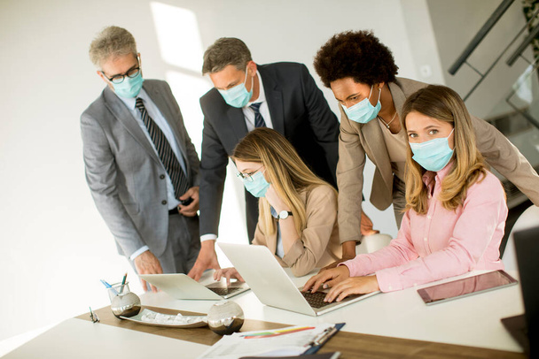 Grup iş adamlarının ofiste bir toplantısı var ve Corona virüsünden korunmak için maske takıyorlar. - Fotoğraf, Görsel