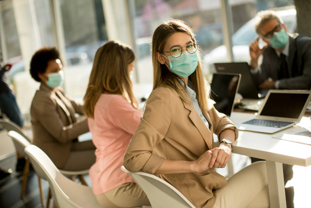 Pretty young woman and group business people have a meeting and working in the office and wear mask as protection from corona virus - Photo, image