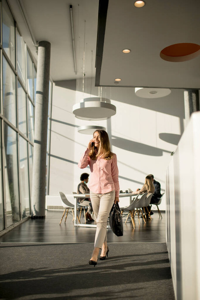Joven mujer de negocios en el teléfono celular caminando en la oficina - Foto, Imagen
