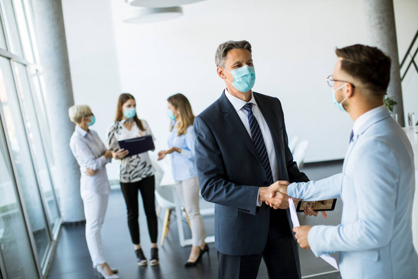 Dois colegas com máscaras ptoectivas aperto de mão quando se encontram no escritório
 - Foto, Imagem