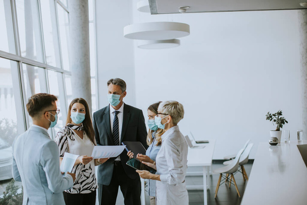 Geschäftspartner stehen im Büro und betrachten Geschäftsergebnisse, während sie Gesichtsmasken als Virenschutz tragen - Foto, Bild