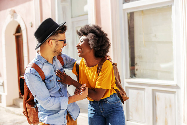 Young attractive happy multiracial couple standing outdoors on a beautiful sunny day flirting on the street. - Foto, imagen