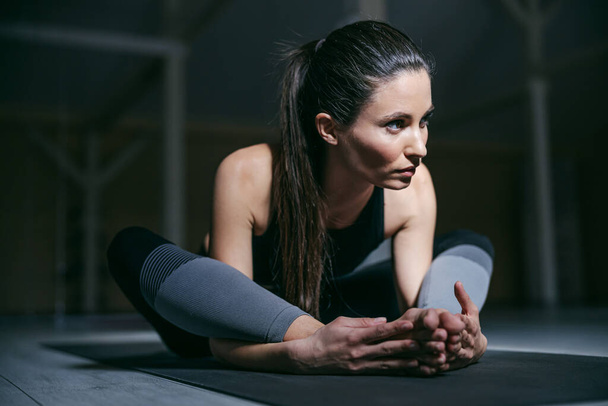 Primo piano di giovane attraente ragazza in forma yogi seduto sul tappeto yoga e fare yoga. - Foto, immagini