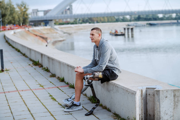 Красивый спортсмен-инвалид в спортивной одежде и с искусственной ногой, сидящей на набережной
. - Фото, изображение