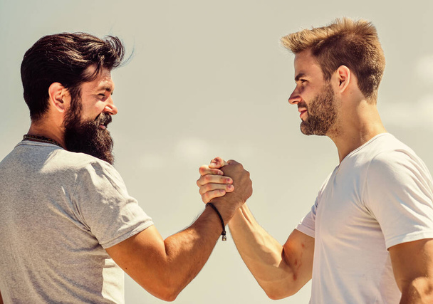 Handshake arm wrestling style. Strong and muscular arms. Successful deal handshake blue sky background. Men shaking hands at meeting. Friendly handshake gesture concept. Friends or competitor - Fotografie, Obrázek
