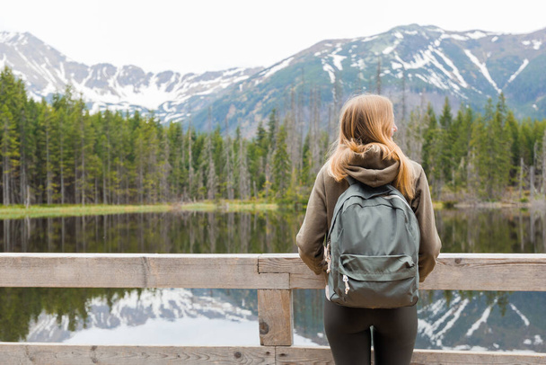 Blonde young girl standing by the mountain lake in the woods. Travel and active life concept. Outdoors - Photo, Image