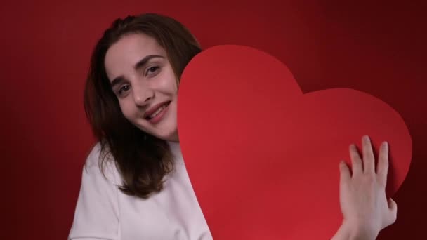 The concept of Valentines Day and Womens Day. Happy young girl holding a big red heart in her hands. A romantic gift. - Video