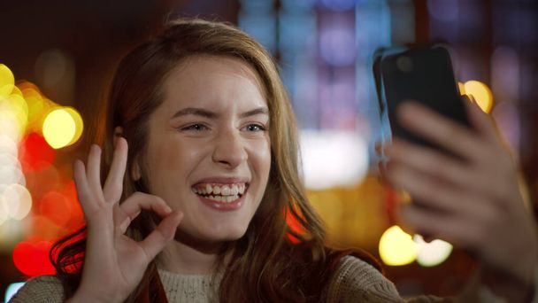 Uśmiechnięta kobieta robiąca selfie przez telefon komórkowy. Dziewczyna pokazuje ok gest na zewnątrz - Zdjęcie, obraz