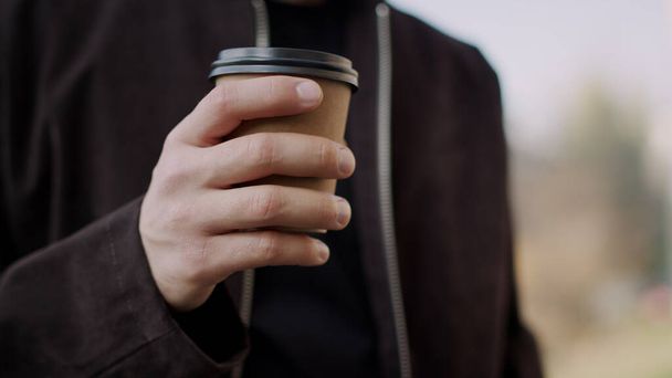 Mano de hombre trayendo café para llevar a los labios. Chico mano sosteniendo papel taza al aire libre
. - Foto, imagen