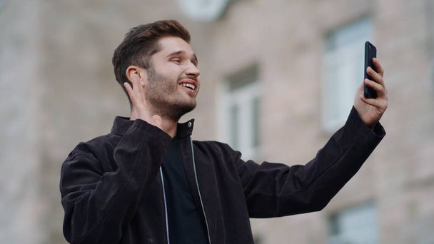 Uśmiechnięty mężczyzna patrzący na ekran telefonu. szczęśliwy facet mając wideo rozmowy na ulicy - Zdjęcie, obraz