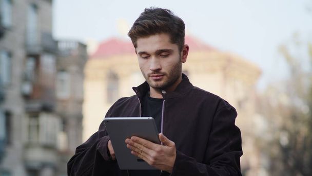 Genç adam dışarıda tablet kullanıyor. Hippi görünümlü cihaz ekranı açık havada. - Fotoğraf, Görsel