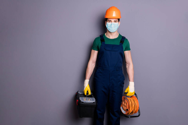 Portrait of his he attractive healthy guy workman wearing safety gauze protective mask contagious viral pneumonia mers cov infection prevention carrying tools isolated grey color background - 写真・画像