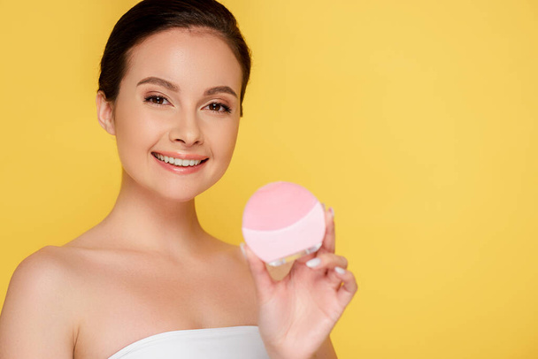 smiling beautiful woman holding facial cleansing brush isolated on yellow - Fotoğraf, Görsel