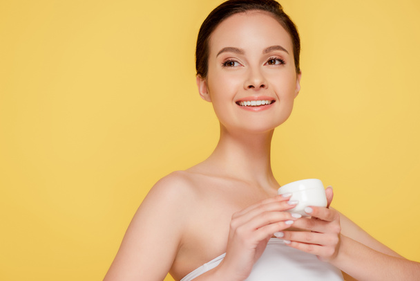 smiling beautiful woman holding container with cosmetic cream isolated on yellow - Valokuva, kuva