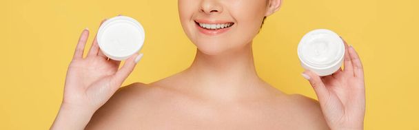 cropped view of smiling beautiful naked woman holding container with cosmetic cream isolated on yellow, panoramic shot - Zdjęcie, obraz