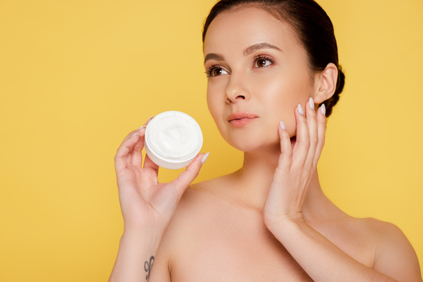beautiful naked woman holding container with cosmetic cream isolated on yellow - Φωτογραφία, εικόνα